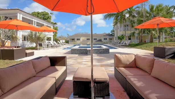 Zona de piscina con mobiliario exterior y sombrillas.