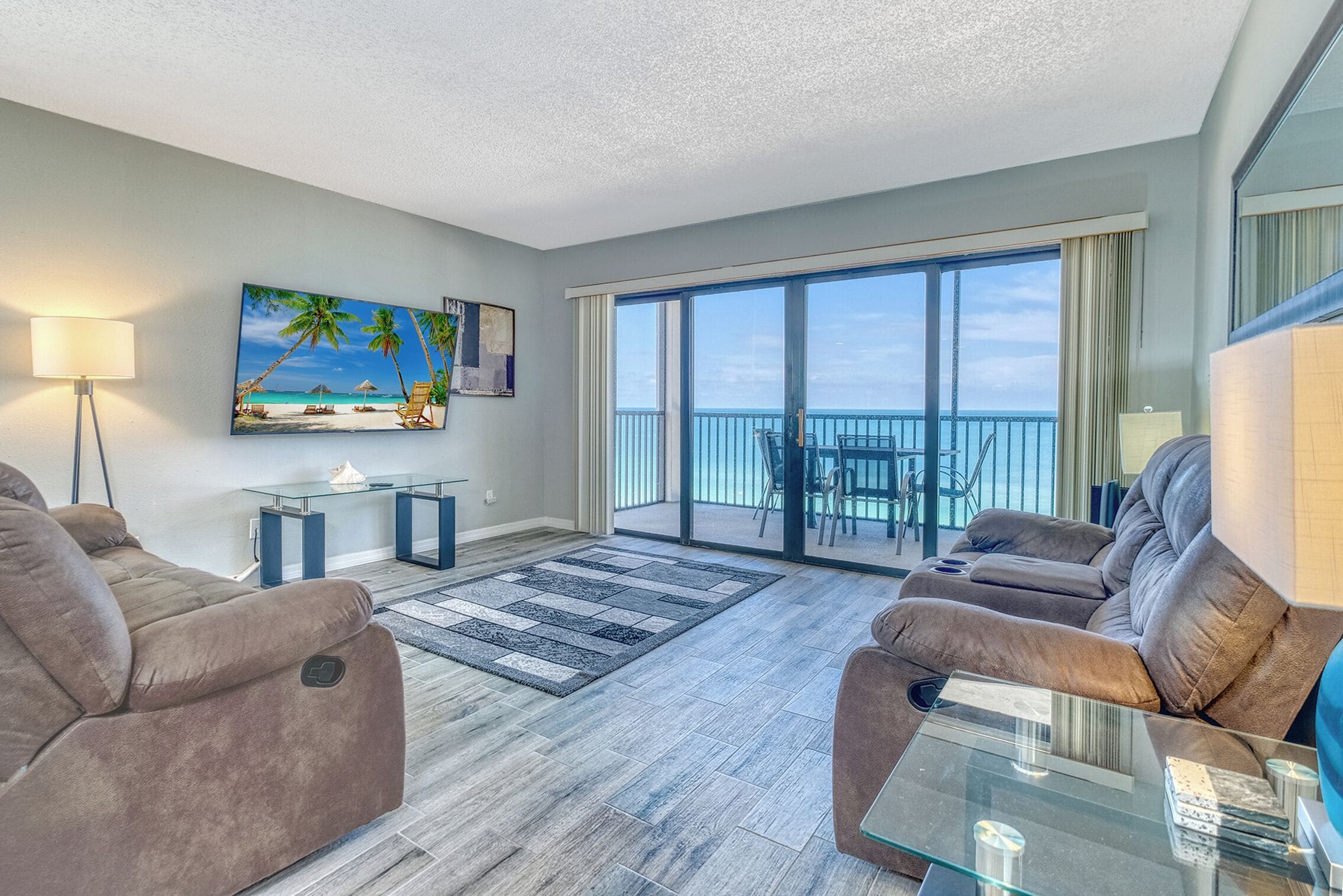 A modern living room with a large window, a sofa set, a coffee table, and a painting of a beach scene.