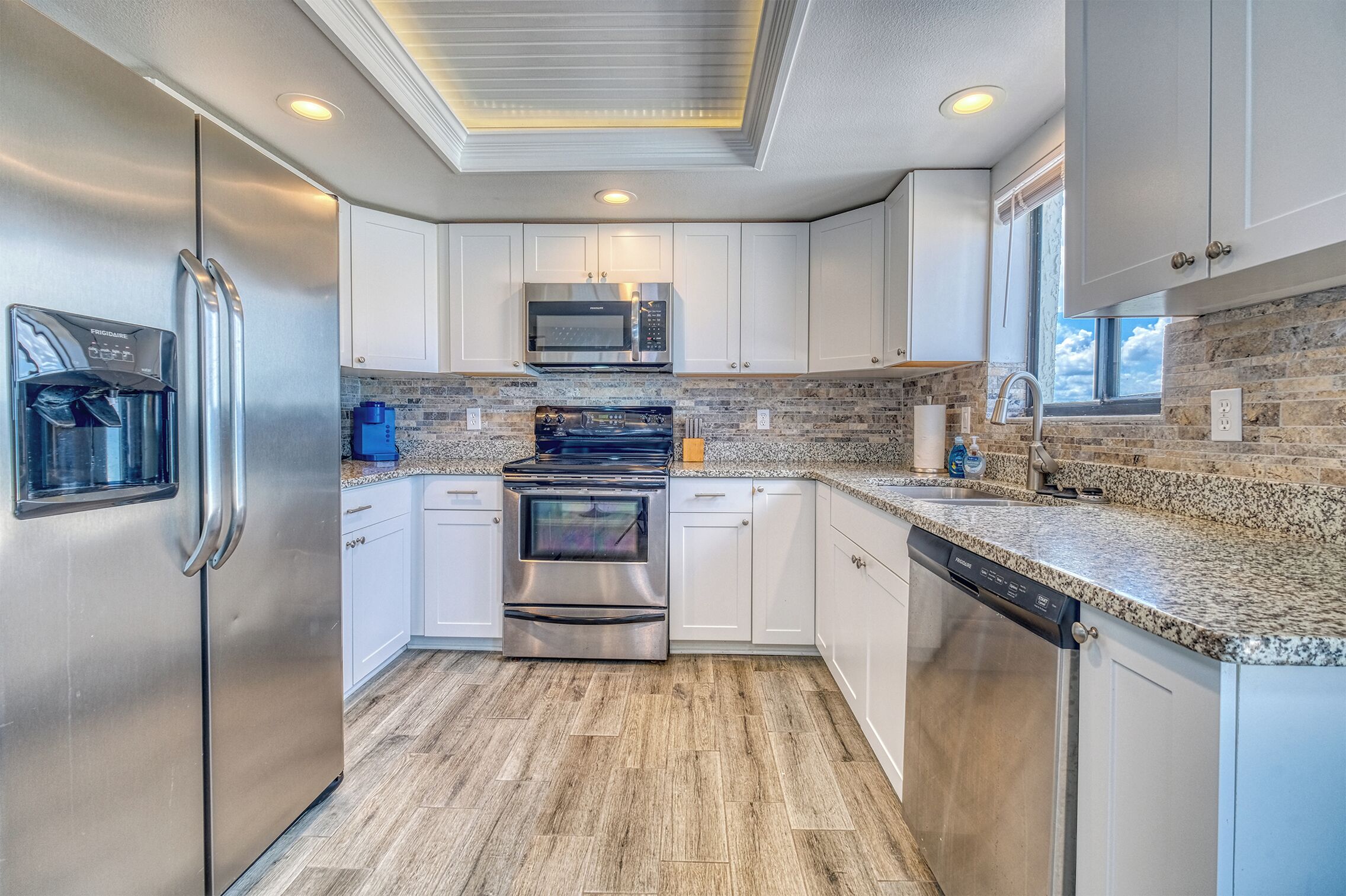 A modern kitchen with stainless steel appliances, white cabinetry, and a granite countertop.