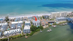 Luftaufnahme einer Küstenhotelanlage mit mehreren Gebäuden, einem Yachthafen und einem Strand.