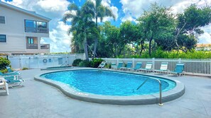 Una piscina amb una tanca blanca, seients de bany i un edifici al fons.