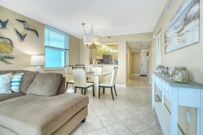 A living room with a sofa, dining table, chairs, and a kitchen area in the background. - Two Bedroom/Two Bathroom Direct Intracoastal Condo (Indian Shores)