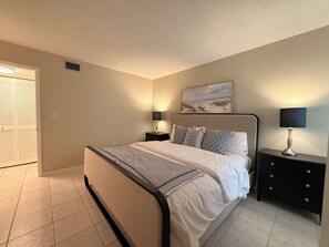 Een slaapkamer met een bed, twee nachtkastjes, een wandlamp en een deur met een raam.