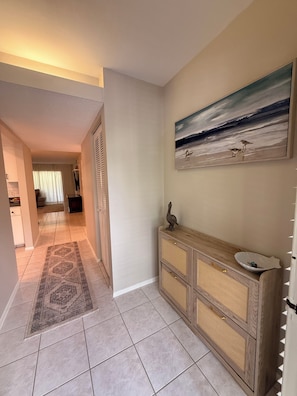 A hallway with a patterned rug, a wooden console with a sink, and a painting of birds on the wall.