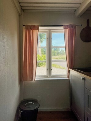Um quarto pequeno com janela, uma lixeira e um armário.