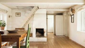 A room with a wooden floor, a fireplace, a dining table with chairs, a staircase, and a white door.