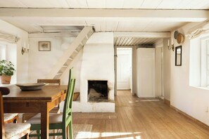 A room with a wooden floor, a fireplace, a dining table with chairs, a staircase, and a white door.