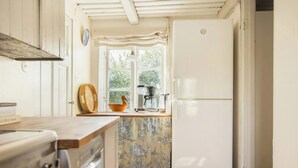 A kitchen with a white refrigerator, a coffee machine, and a window with a view of greenery. - Scanian longhouse with studio in Österlen (Smedstorp Tomelia)