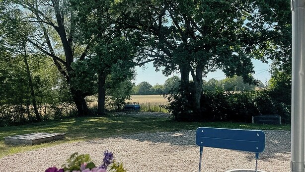 A table with a vase of flowers, a bench, and a view of a field with trees. - Scanian longhouse with studio in Österlen (Smedstorp Tomelia)