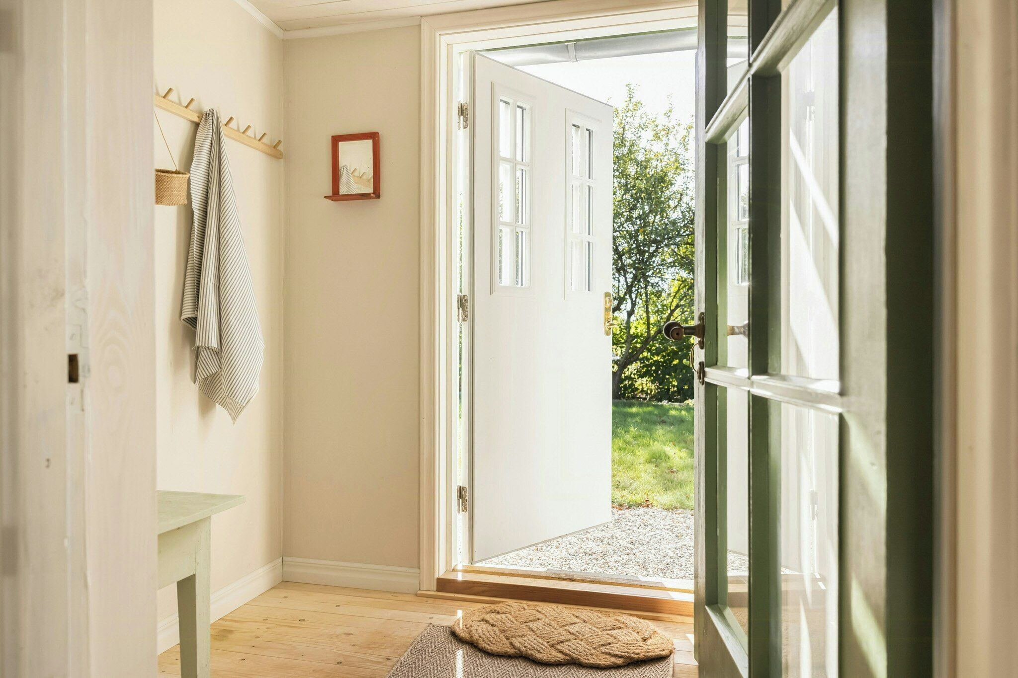A hallway with a coat rack, a framed picture, and a door leading outside.