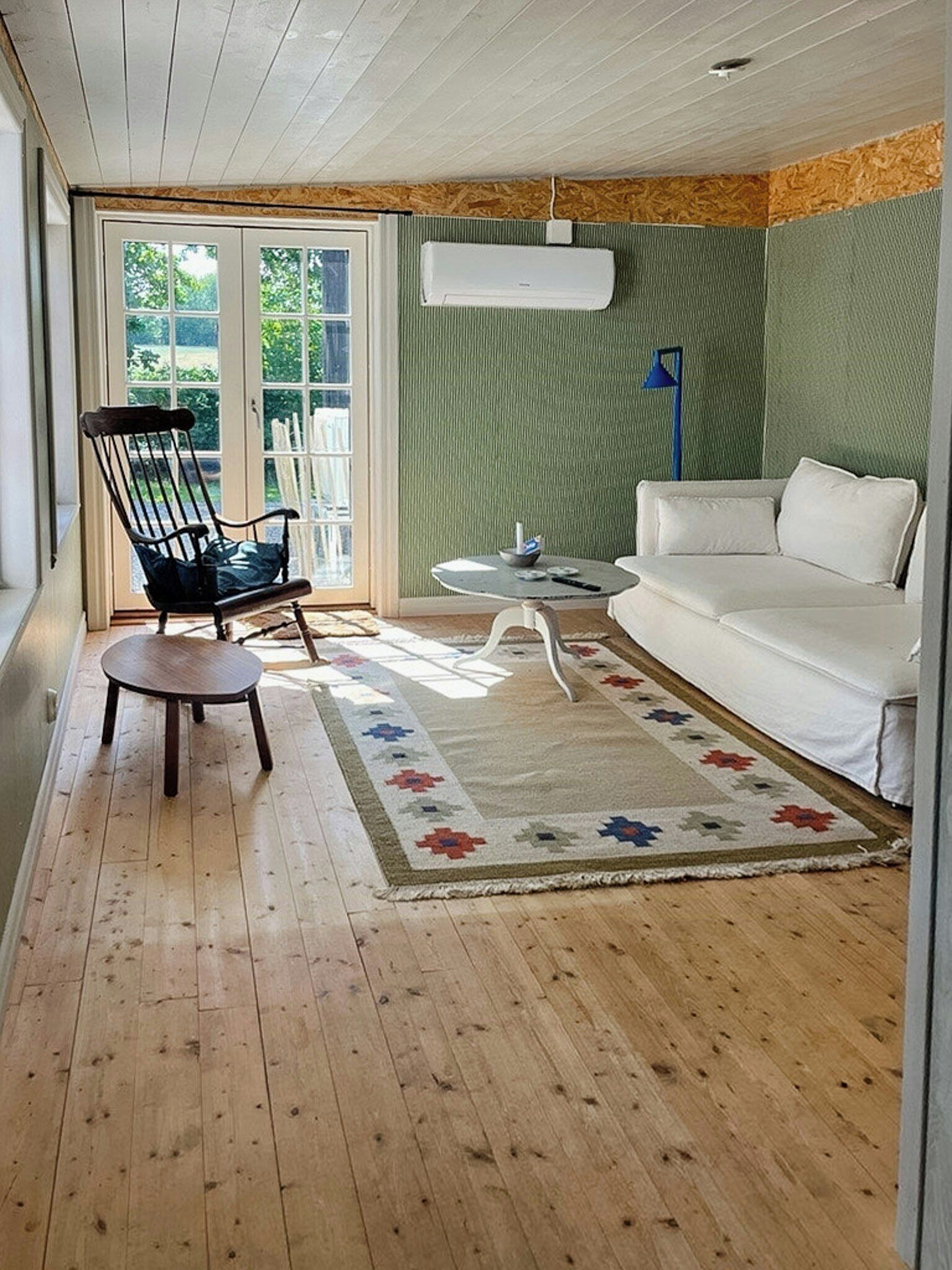 A room with a wooden floor, a white sofa, a black chair, a small round table, and a patterned rug.