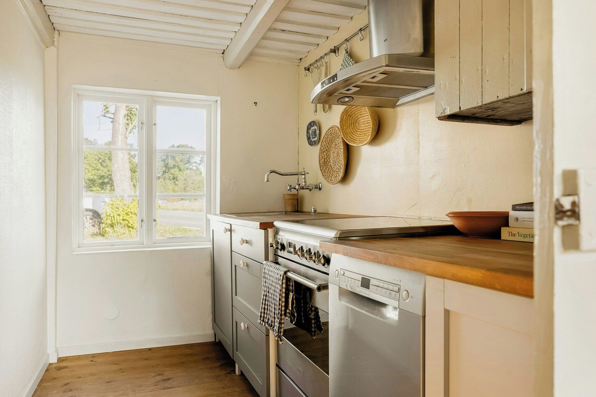 A kitchen with a built-in oven, a dishwasher, and a window with a view of greenery.