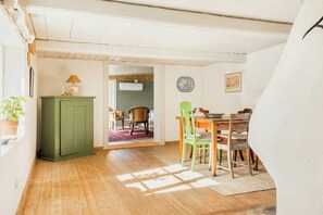 A room with a wooden floor, a green cabinet, a dining table with chairs, and a doorway leading to another room. - Scanian longhouse with studio in Österlen (Smedstorp Tomelia)
