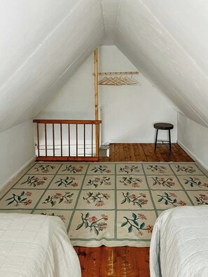 Um quarto de sótão pequeno com teto inclinado, soalho de madeira, uma única cadeira de madeira e um cabideiro.