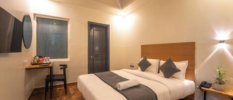 Habitación de hotel con cama, escritorio, silla, una mesita con teléfono y planta, y una puerta.
