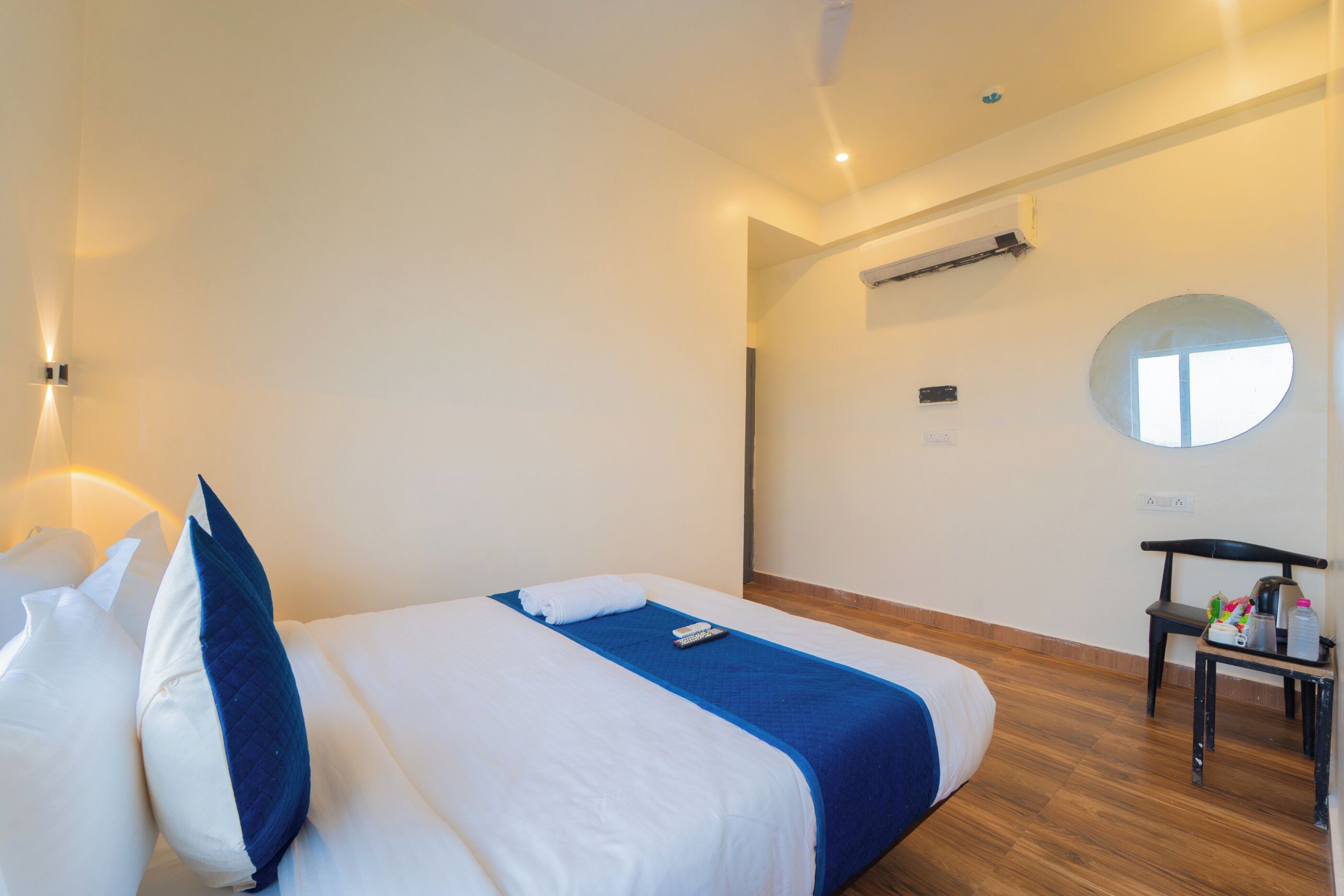 Habitación de hotel con cama, una silla, una mesita y un espejo en la pared.