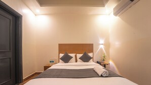 Une chambre d’hôtel comprenant un lit, des tables de chevet, une petite table, une lampe fixée au mur et une porte.