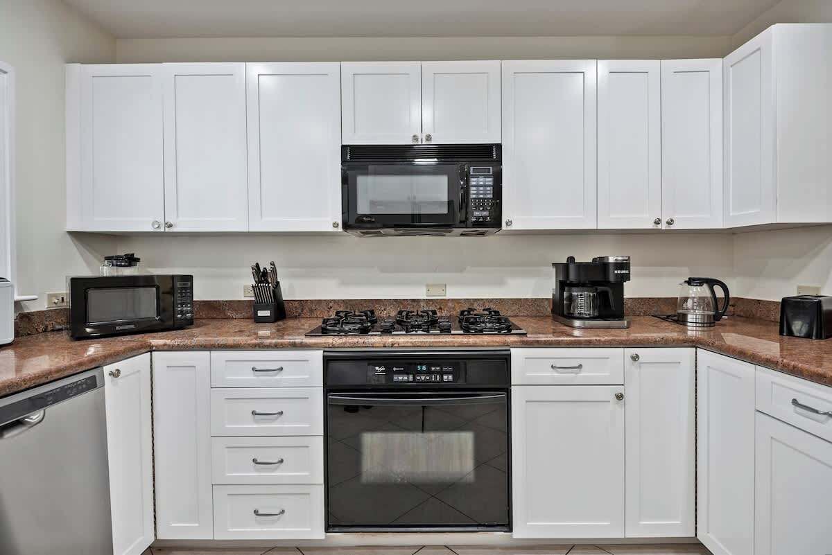 A kitchen with white cabinets, a microwave, stove, dishwasher, and coffee maker.