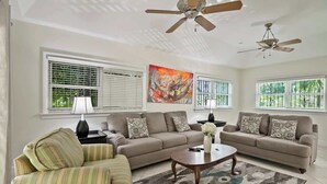 A living room with two sofas, a coffee table, and a striped armchair. There are ceiling fans, a painting, and windows with blinds. - Fully Equipped 3 BR Villa w/ Easy Beach Access (Nassau)