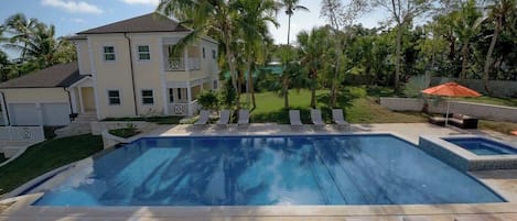 A swimming pool with lounge chairs, palm trees, and a house in the background.