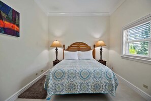 Ein Schlafzimmer mit einem Bett, zwei Nachttischlampen, einem Fenster mit Jalousien, einem Teppich und einem Wandbild.