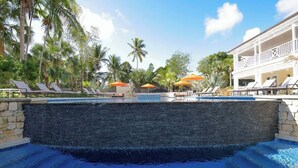 A swimming pool with lounge chairs and umbrellas, surrounded by palm trees and a building with a balcony. - Comfortable Villa Near Beach + Atlantis + Downtown (Nassau)