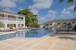 Un espace piscine avec des chaises longues, une terrasse carrelée et un bâtiment doté de balcons.