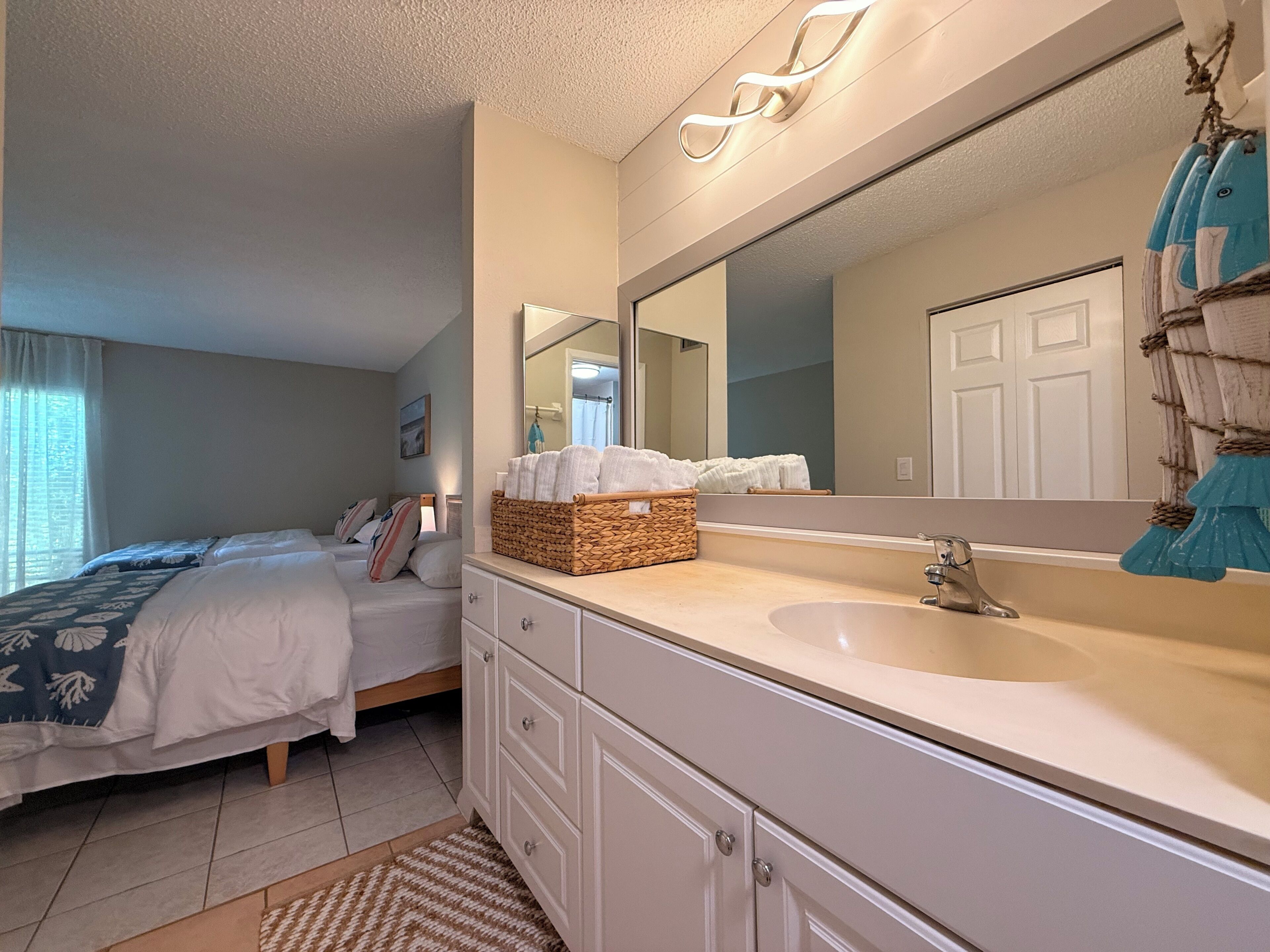 A bedroom with a bed, a bedside table, a mirror, and a bathroom with a sink and mirror.