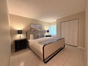 Ein Schlafzimmer mit einem Bett, zwei Nachttischen, einem Fenster mit Vorhängen und einem Kleiderschrank.