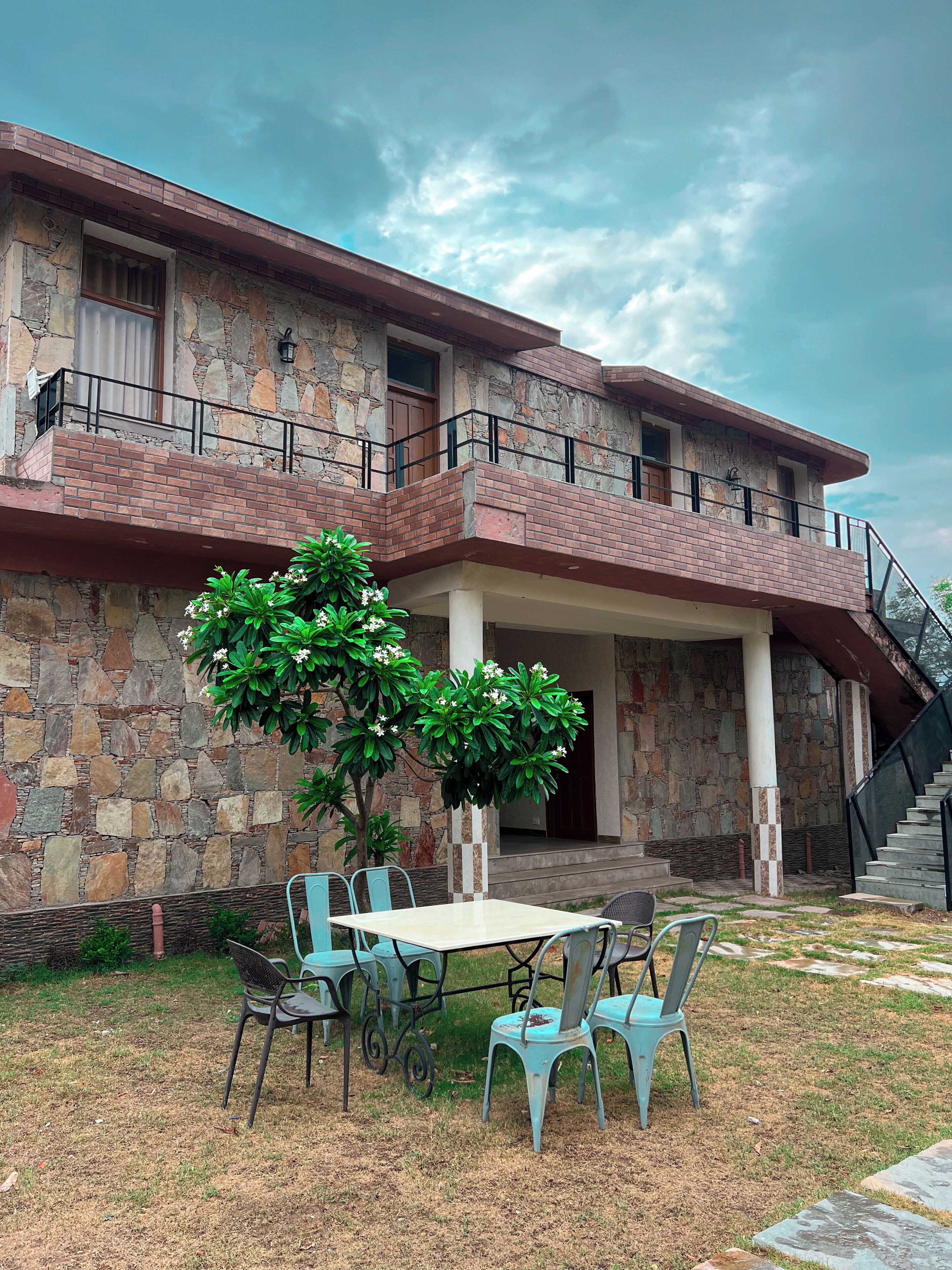 A two-story stone building with a balcony, outdoor seating area, and a staircase.