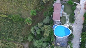 Vista aérea de una propiedad con piscina, zona pavimentada y abundante vegetación.