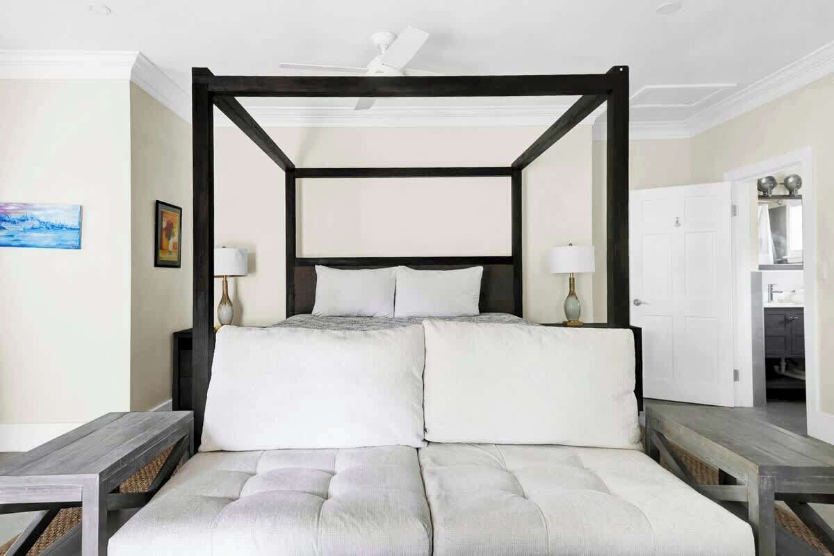 Una cama con dosel tapizada con ropa de cama blanca, un cabecero de madera y dos mesitas de noche con lámparas.