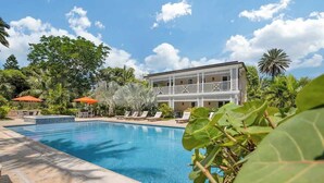 A pool with lounge chairs, a building with balconies, and tropical vegetation. - Spacious Studio Near Atlantis Equipped w/ Kitchen (Nassau)