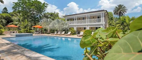 Une piscine avec des chaises longues, un bâtiment doté de balcons et une végétation tropicale.