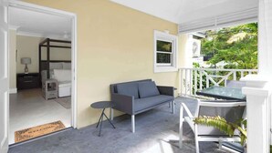 A room with a sofa, a small table, and a view of greenery outside. - Silk Cotton Studio 3 (Nassau)