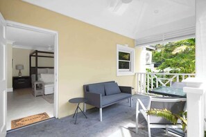 A room with a sofa, a small table, and a view of greenery outside. - Silk Cotton Studio 3 (Nassau)
