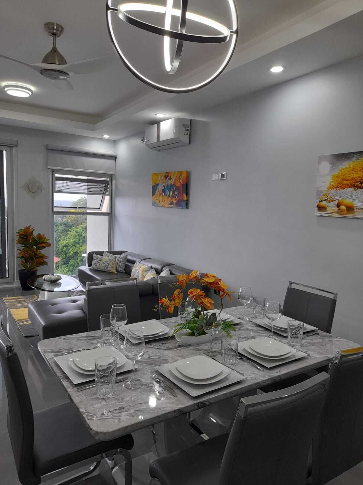 Un comedor moderno con una mesa de mármol dispuesta para cuatro personas, rodeado de sillas oscuras.