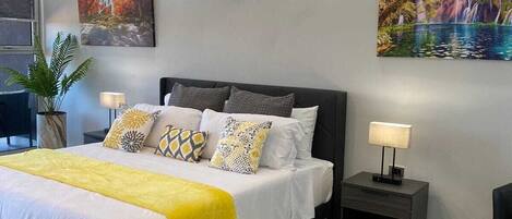 Une chambre à coucher moderne, avec un lit, des tables de chevet, un climatiseur fixé au mur et un tableau.