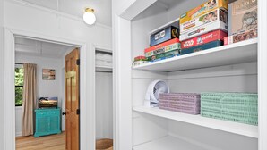 A room with a wooden door, a teal cabinet, a wicker basket, and a white shelf with board games. - Pet-Friendly Cottage w/ Golf Cart, Kayak & Easy Beach Access (Emerald Isle)