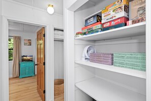 A room with a wooden door, a teal cabinet, a wicker basket, and a white shelf with board games. - Pet-Friendly Cottage w/ Golf Cart, Kayak & Easy Beach Access (Emerald Isle)