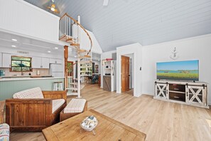 A spacious living area with a wooden staircase, a dining area, and a kitchen with a view. - 3BR Oceanside with Easy Beach Access | Golf cart + Pet Friendly (Emerald Isle)