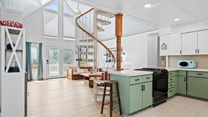 A spacious kitchen with a central island, wooden bar stools, and a spiral staircase. - Pet-Friendly Cottage w/ Golf Cart, Kayak & Easy Beach Access (Emerald Isle)