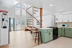 A spacious kitchen with a central island, wooden bar stools, and a spiral staircase. - Pet-Friendly Cottage w/ Golf Cart, Kayak & Easy Beach Access (Emerald Isle)