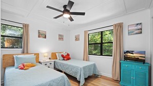 A room with two beds, a ceiling fan, a TV on a cabinet, and artwork on the walls. - Pet-Friendly Cottage w/ Golf Cart, Kayak & Easy Beach Access (Emerald Isle)