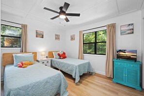 A room with two beds, a ceiling fan, a TV on a cabinet, and artwork on the walls. - Pet-Friendly Cottage w/ Golf Cart, Kayak & Easy Beach Access (Emerald Isle)
