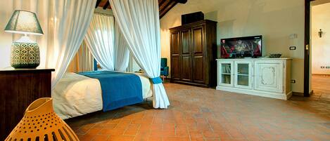 A bedroom with a four-poster bed, a television on a cabinet, and a chair.