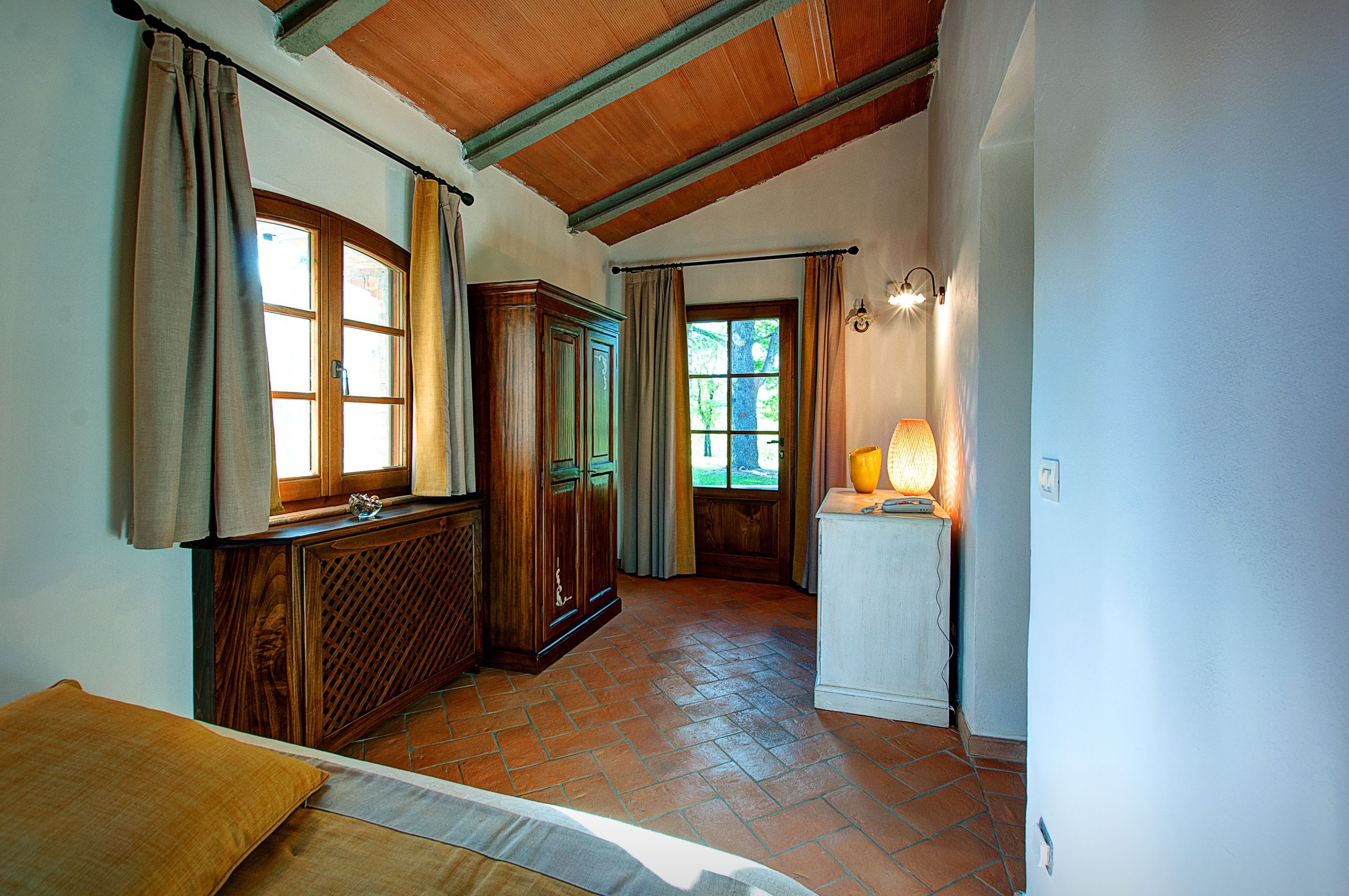 A room with a wooden cabinet, a radiator, a bed with a pillow, and a lamp on a table.