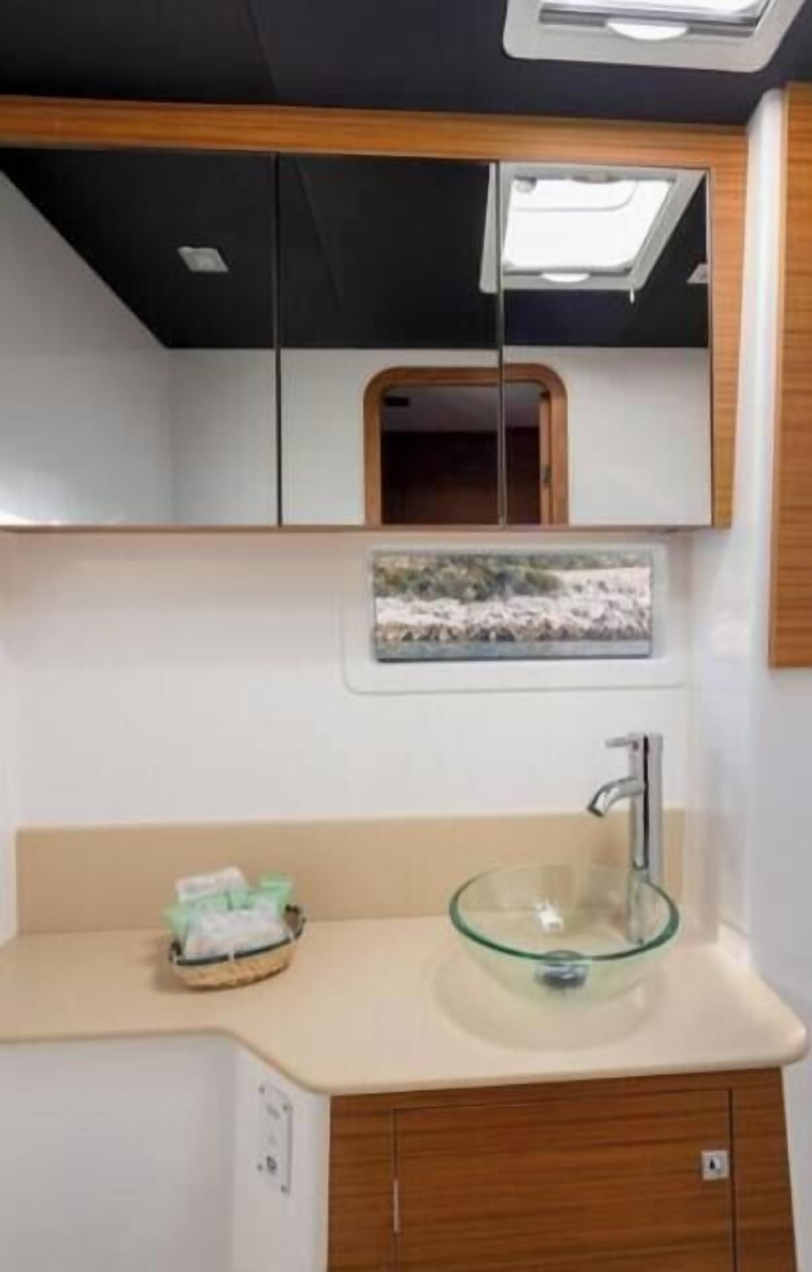 A bathroom with a glass sink, a mirror above it, and a small window with a view.