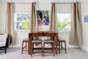 A room with a wooden desk, two chairs, a window with blinds, and a painting on the wall. - 1 BR Studio w/ King Bed + Easy Beach Access (Nassau)
