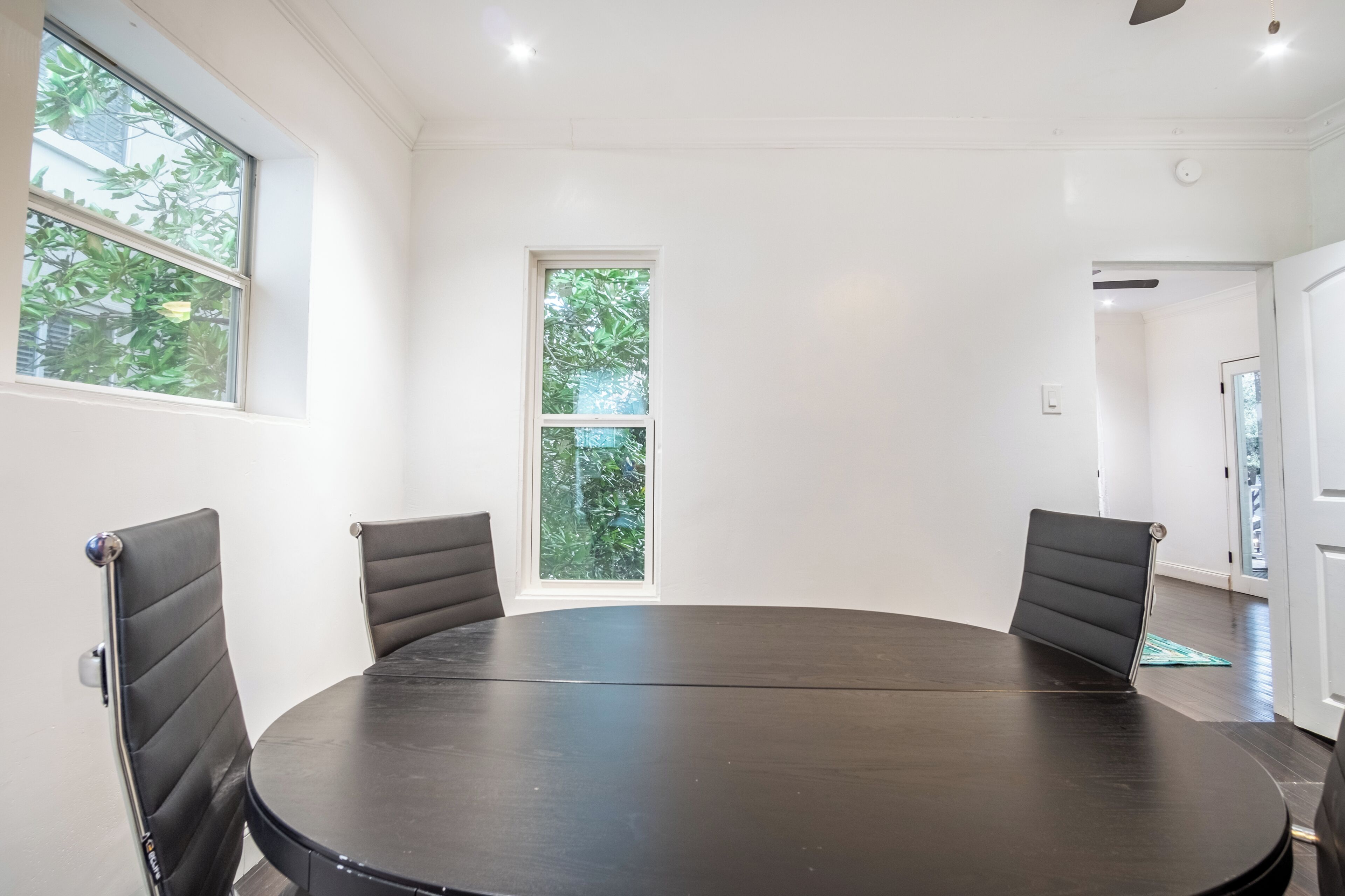 A conference room with a round table, four chairs, and large windows with a view of greenery.